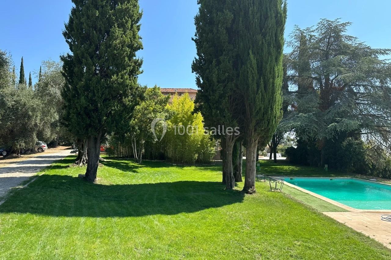 Jardin avec pelouse, arbres imposants et piscine sur la droite, sous un ciel bleu dégagé.