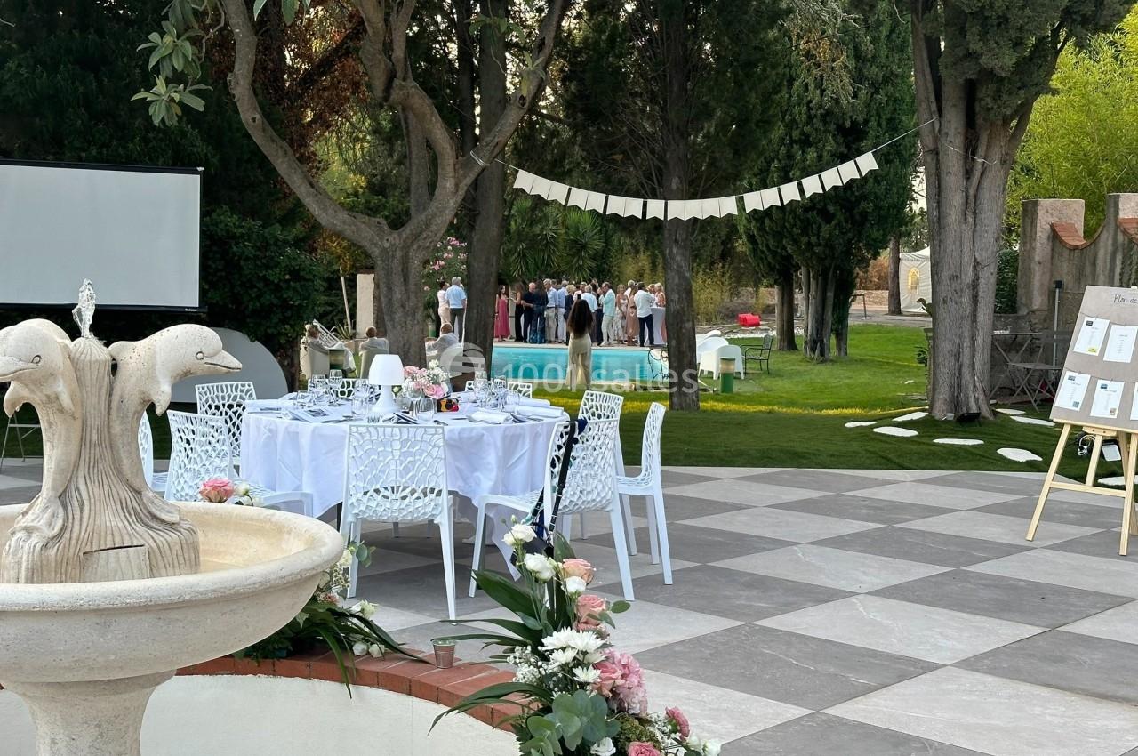 Espace extérieur décoré pour un événement, avec tables dressées, fontaine et invités rassemblés près d'une piscine.