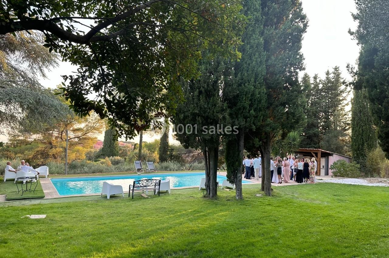Groupe de personnes rassemblées près d'une piscine entourée de pelouse et d'arbres dans un cadre extérieur.