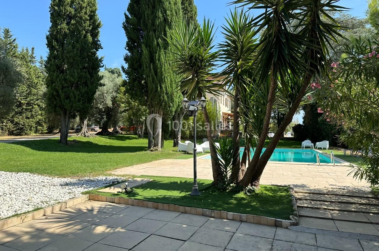 Jardin avec pelouse, arbres, piscine et terrasse en pierre, entouré de végétation sous un ciel dégagé.