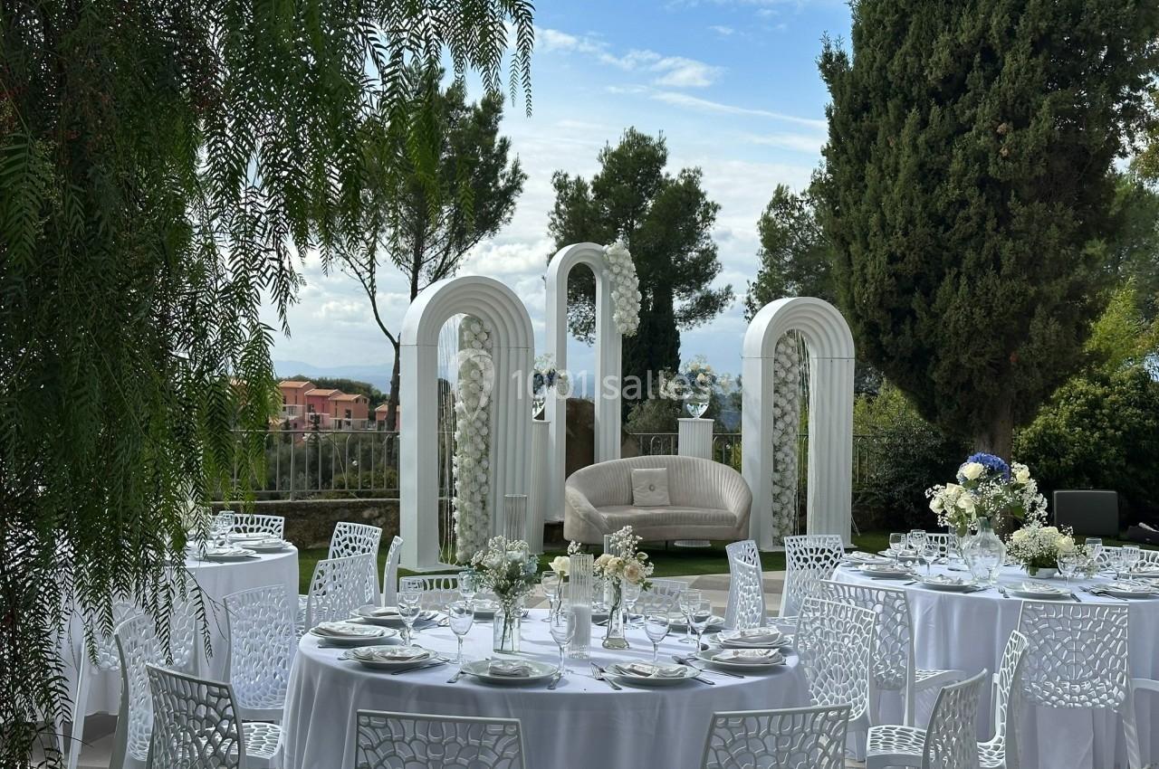 Tables rondes décorées pour un événement en extérieur, avec des arches blanches et un canapé en arrière-plan.