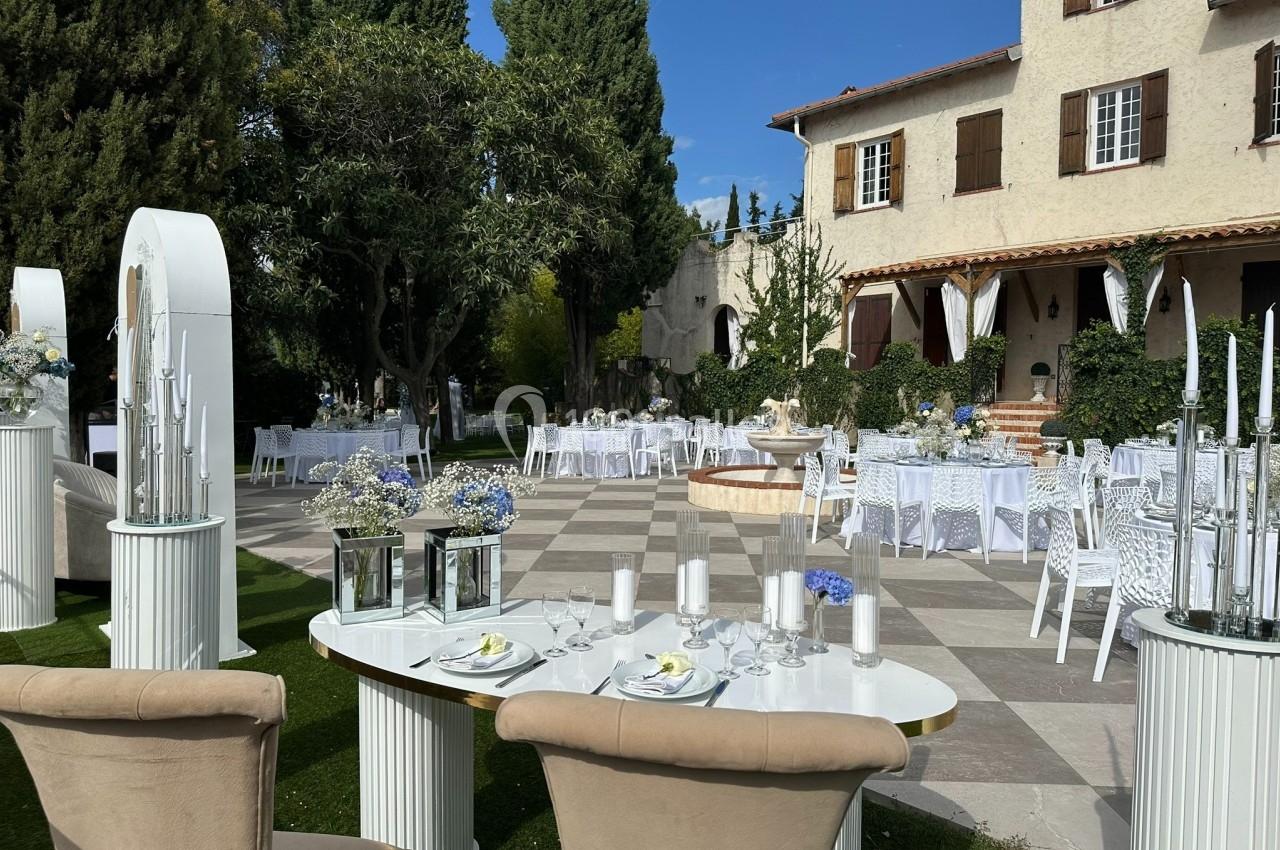 Tables décorées pour un événement en plein air dans une cour avec fontaine, entourée d'arbres et d'un bâtiment en arrière…