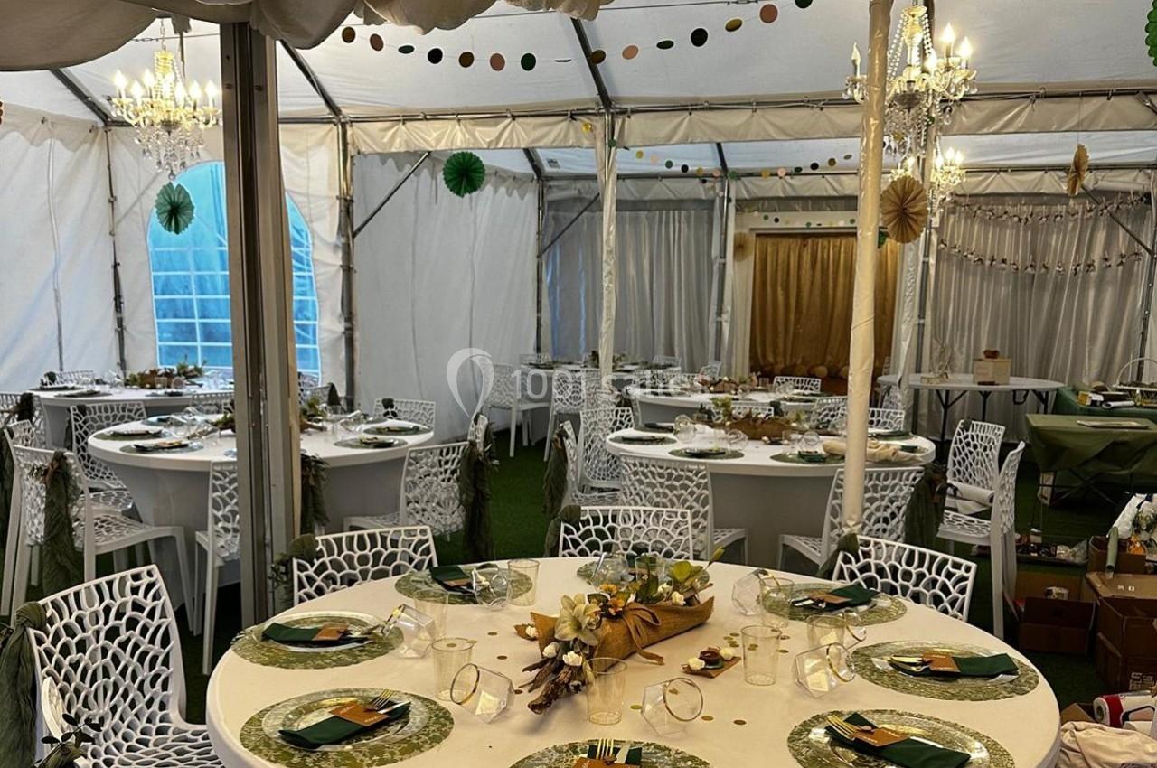 Salle de réception sous tente avec tables rondes décorées de manière festive et lustres suspendus.