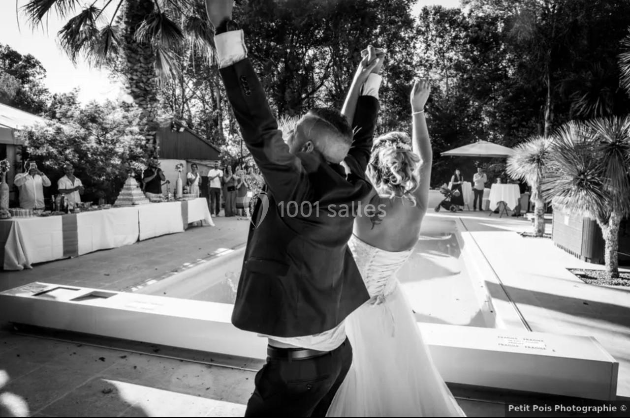 Un couple de mariés lève les bras en l'air devant des invités lors d'une réception en extérieur près d'une piscine.