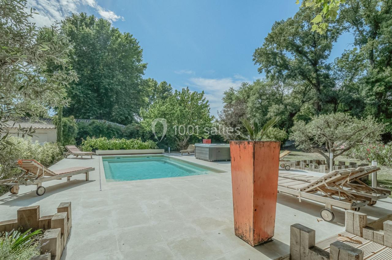 Terrasse avec piscine entourée de chaises longues, végétation luxuriante et grand pot de fleurs orange au premier plan.