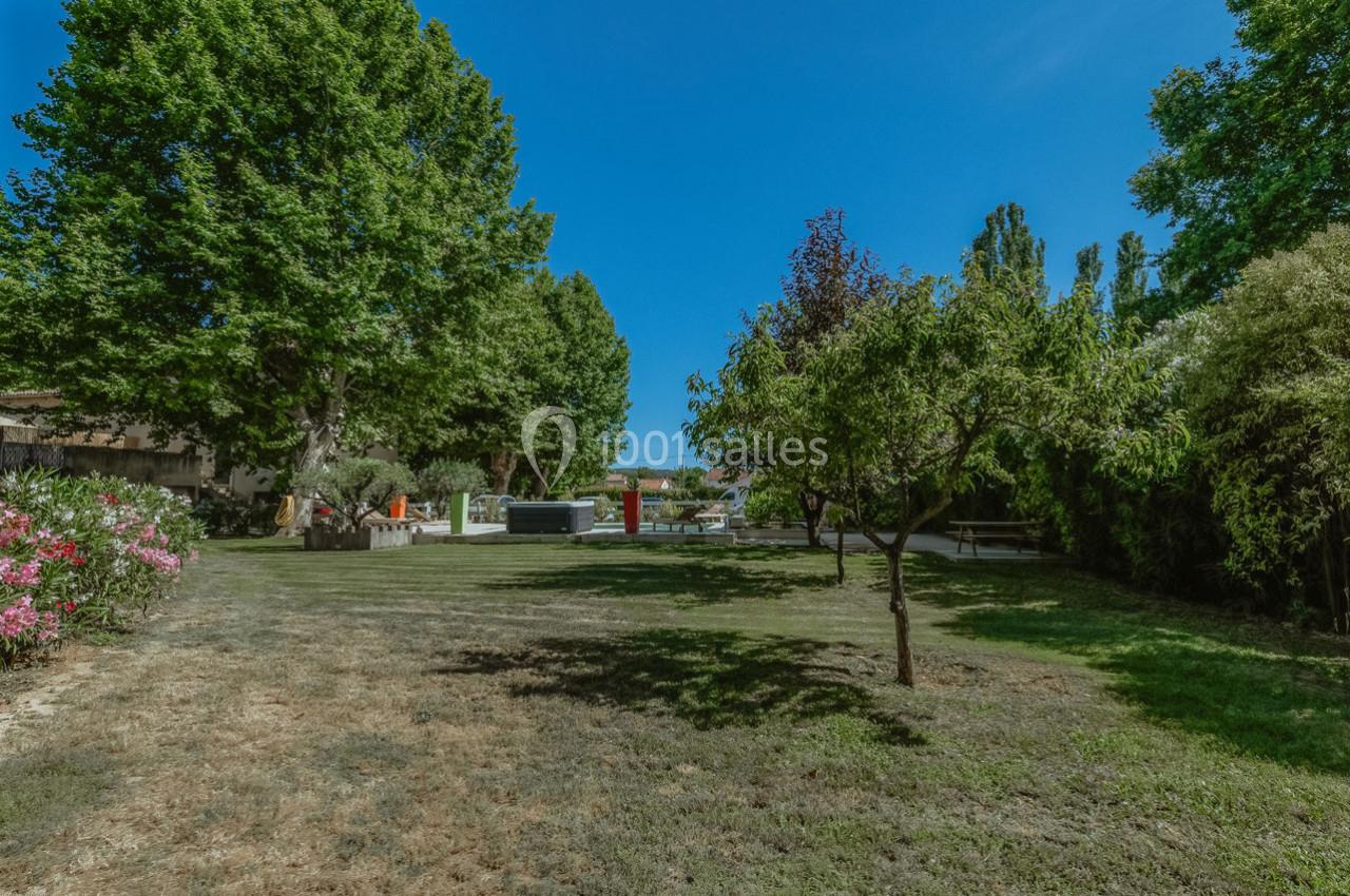 Jardin arboré avec pelouse, arbres variés et mobilier extérieur, sous un ciel bleu dégagé.