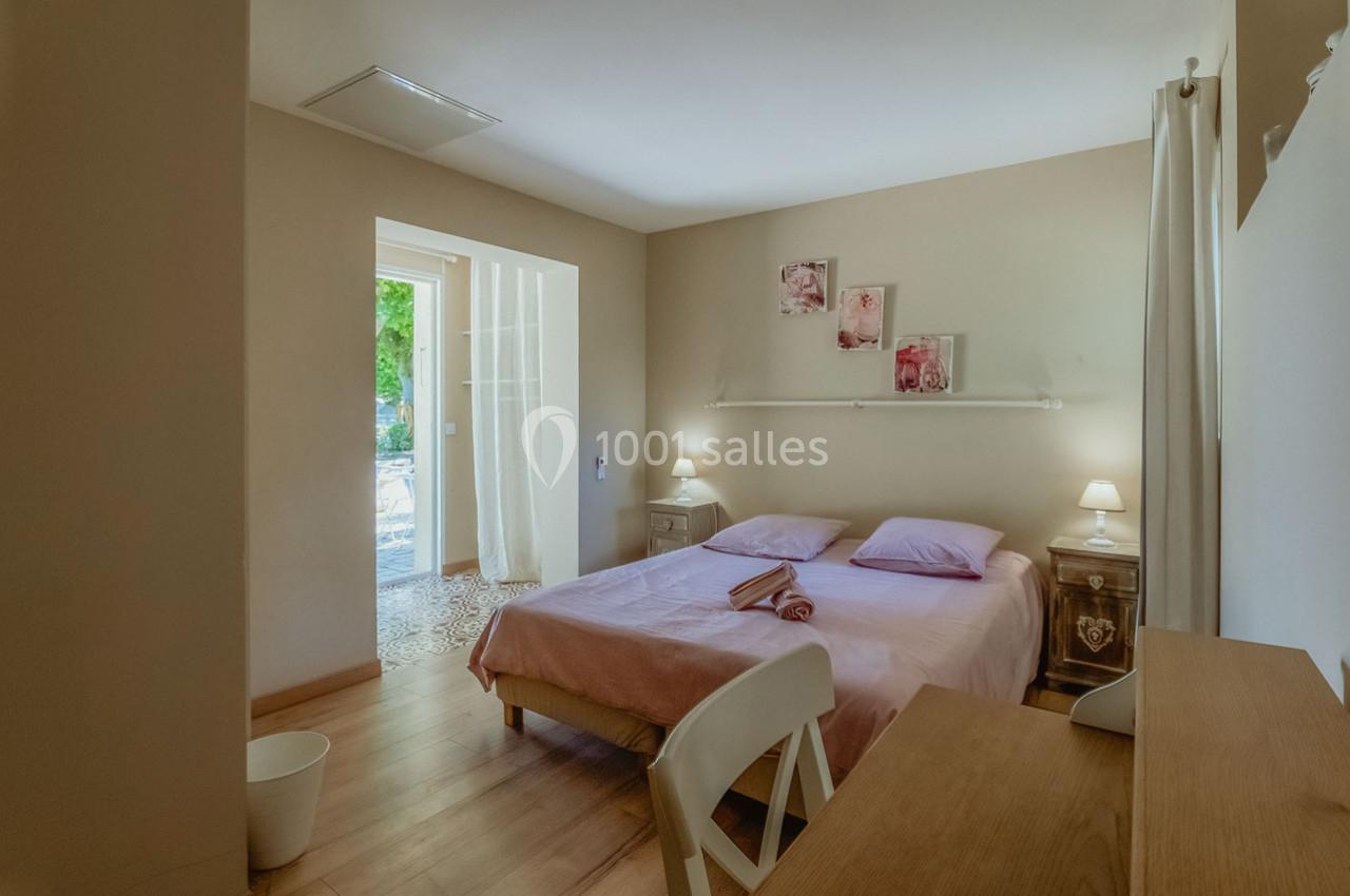 Chambre lumineuse avec lit double, draps roses, deux tables de chevet, et vue sur une terrasse extérieure.