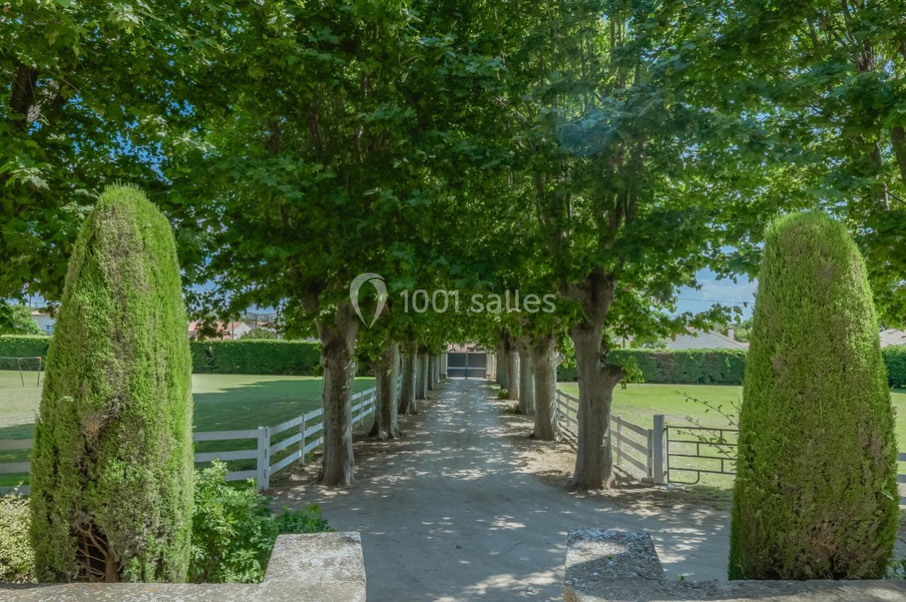Allée bordée d'arbres et de haies, menant à un portail, avec des espaces verts de chaque côté.