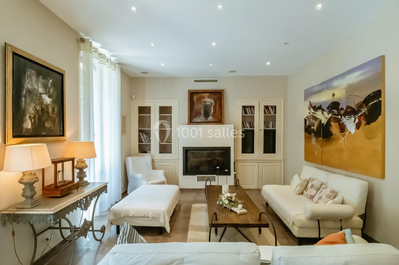 Salon lumineux avec canapés blancs, table basse en bois, tableaux accrochés et éclairage encastré au plafond.