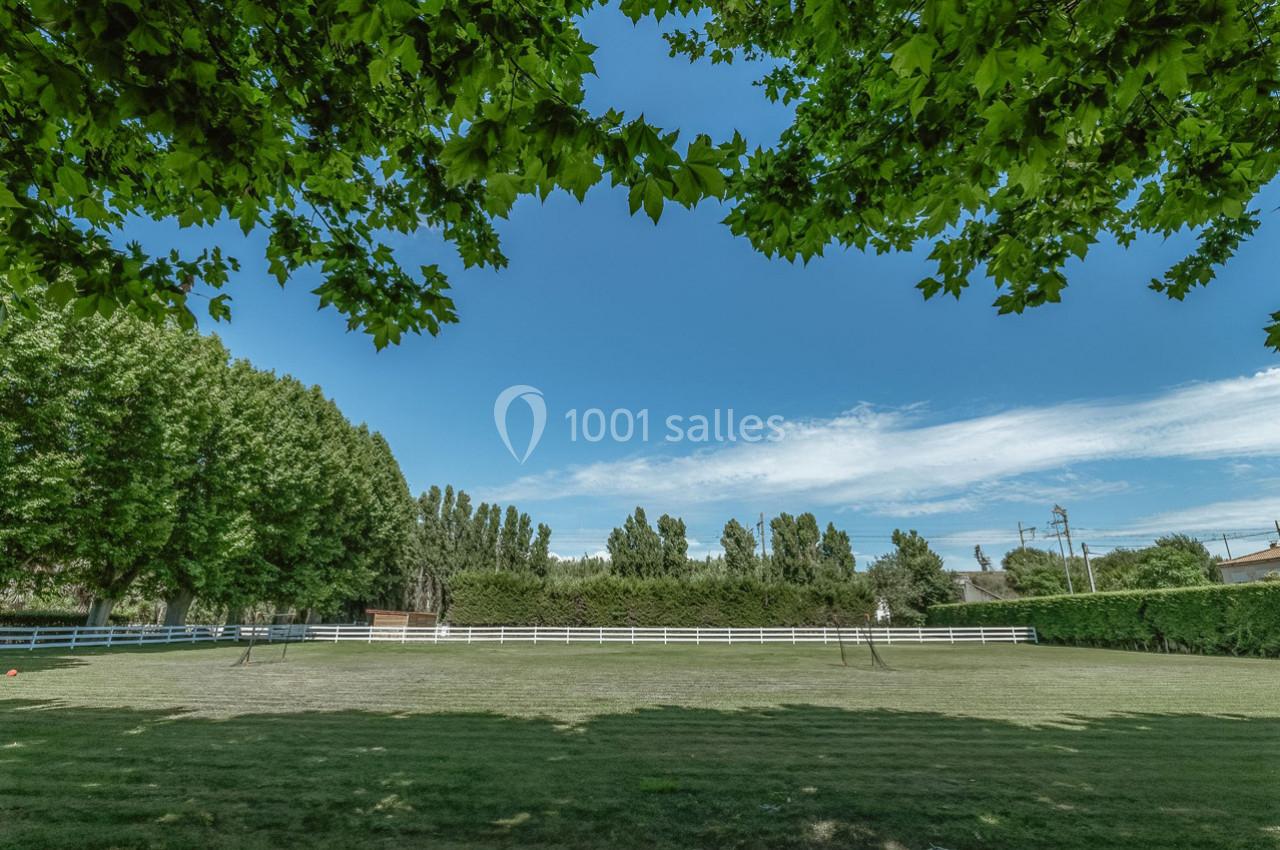 Vue d'un grand espace vert entouré d'arbres, avec une clôture blanche et un ciel bleu dégagé.