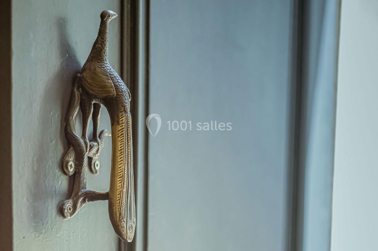 Poignée de porte en forme de paon en métal sculpté, fixée sur une porte en bois sombre.