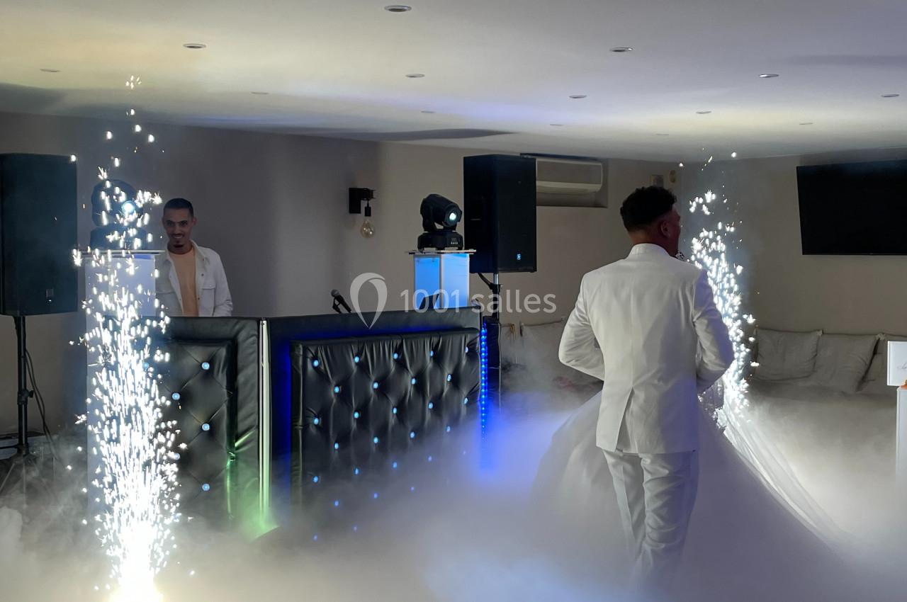 Deux hommes en costume blanc dans une salle avec éclairage d'ambiance, effets de fumée et étincelles.