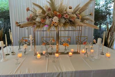 Table décorée avec des bougies allumées, des fleurs séchées et fraîches dans des vases, sur fond de rideaux blancs.