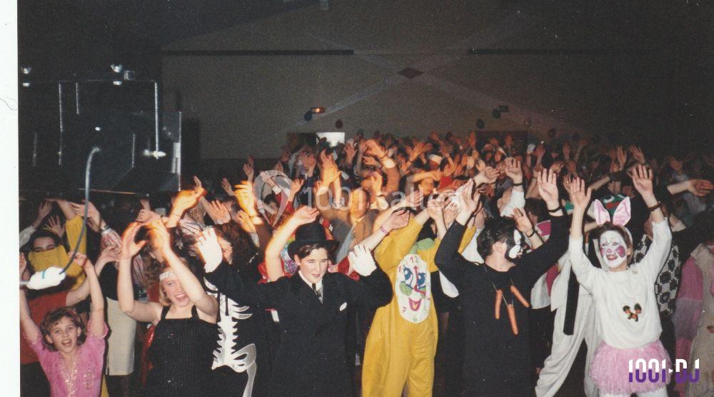 Un groupe de personnes déguisées dansant et levant les bras lors d'une fête ou d'un événement festif en intérieur.