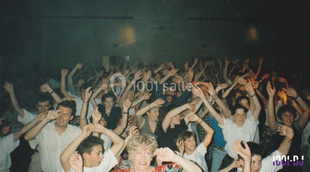 Groupe de personnes dansant et levant les bras lors d'un événement festif dans une salle sombre.
