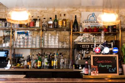 Bouteilles variées alignées sur une étagère en bois dans un bar avec une enseigne ’L'Astrolabe’ en arrière-plan.