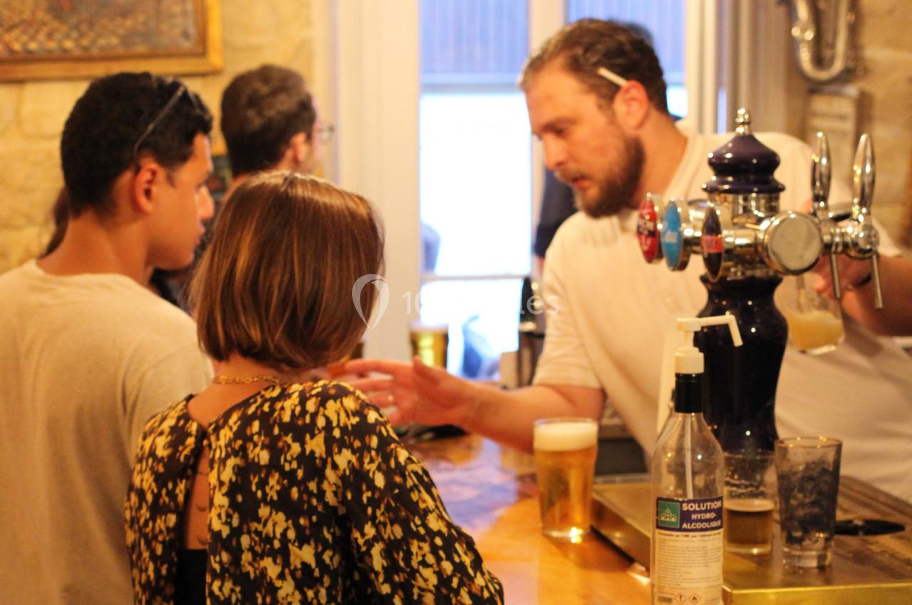 Un barman sert des boissons à des clients dans un bar, avec des verres de bière posés sur le comptoir.