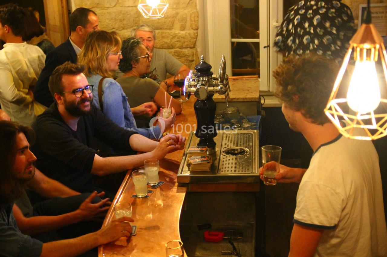 Des personnes discutent et boivent autour d'un comptoir de bar éclairé par des lampes suspendues.