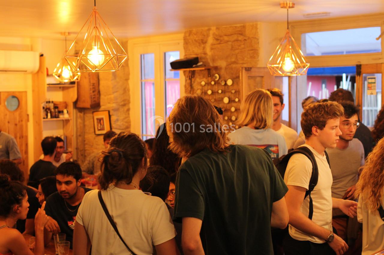Des personnes discutent dans un café animé, éclairé par des suspensions lumineuses et décoré de murs en pierre.
