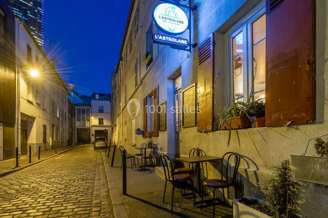 Rue pavée éclairée de nuit avec une terrasse de café vide et une enseigne lumineuse indiquant ’L'Astrolabe’.