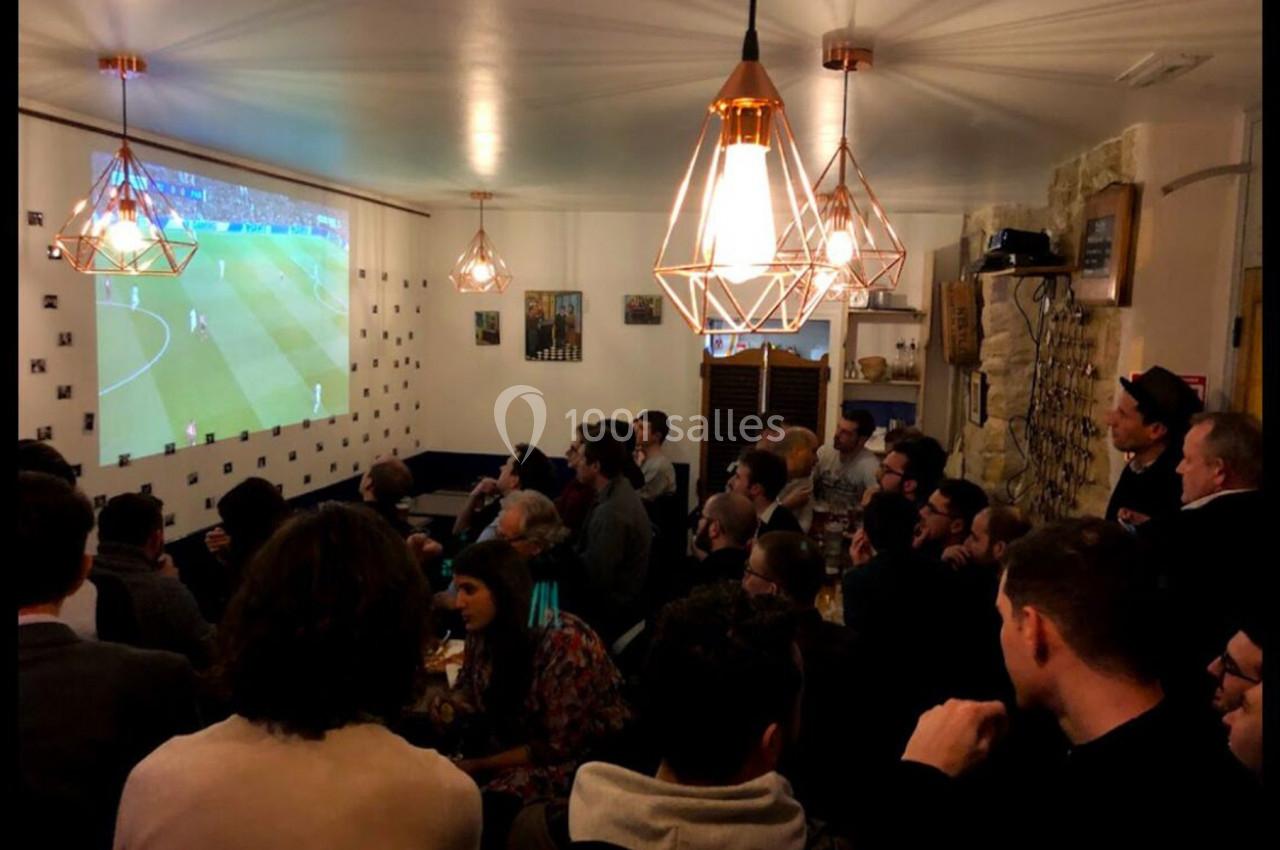 Des personnes rassemblées dans un bar regardent un match de football projeté sur un écran mural.