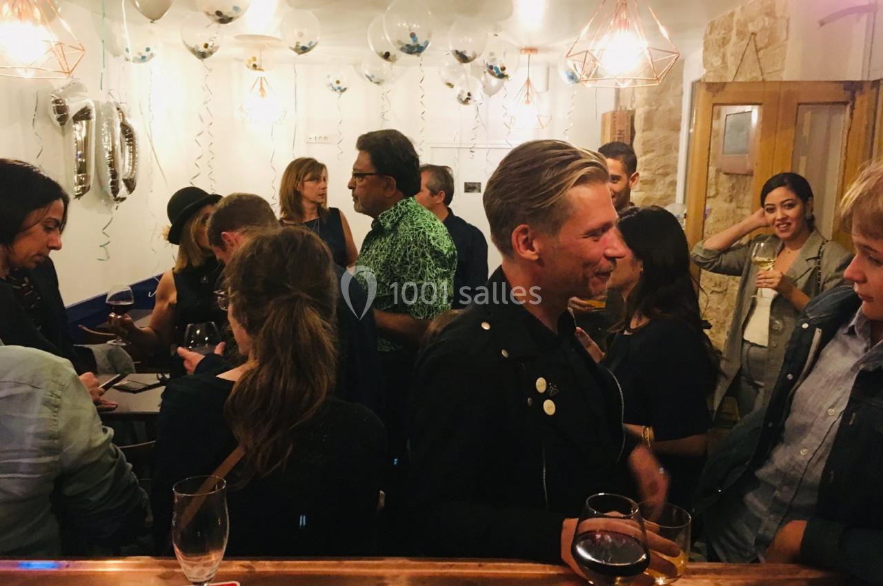 Groupe de personnes discutant dans un bar décoré avec des ballons et des guirlandes, ambiance conviviale.