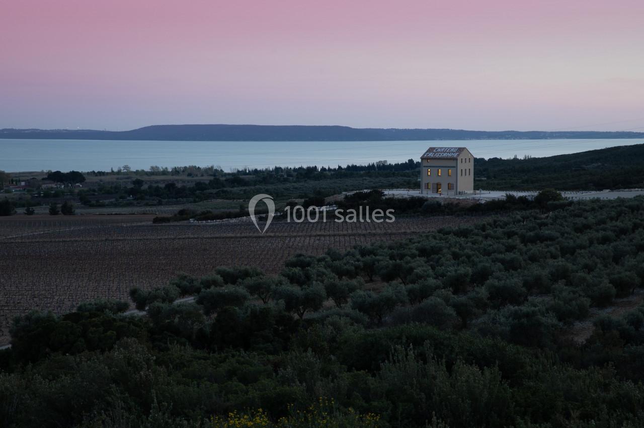 Maison isolée entourée de champs et d'oliviers, avec vue sur un lac au coucher du soleil.