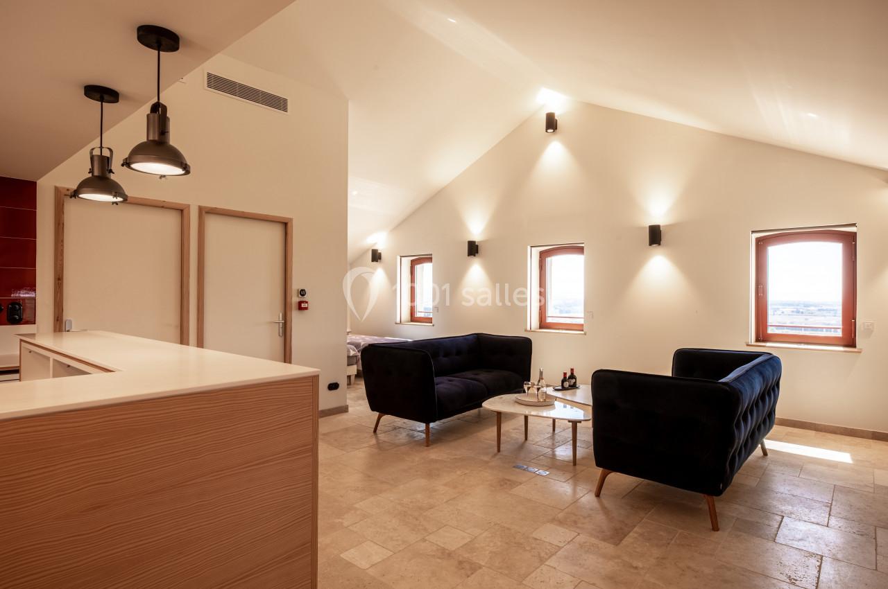 Salon lumineux avec deux canapés noirs, une table basse, des murs blancs et des fenêtres laissant entrer la lumière…