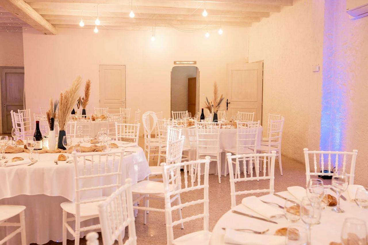 Salle de réception décorée avec des tables rondes, nappes blanches, chaises blanches et centres de table en pampas.