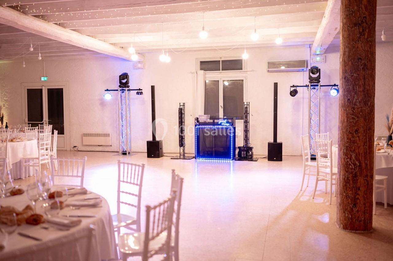 Salle de réception lumineuse avec tables dressées et espace central équipé pour une animation musicale.
