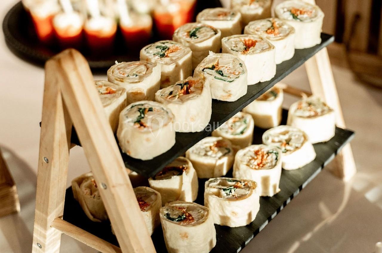 Plateau en bois avec des rouleaux apéritifs garnis de légumes et de fromage, présentés sur deux niveaux.
