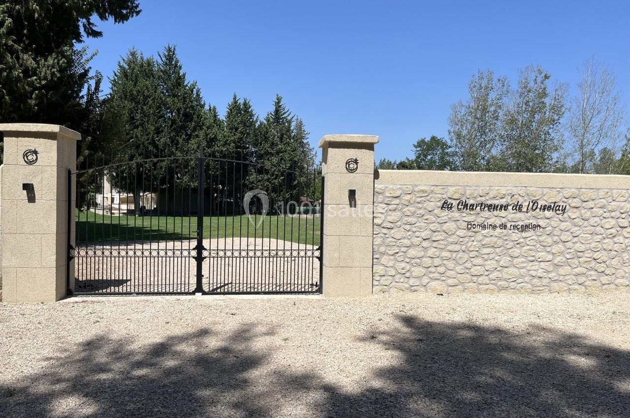 Portail en fer forgé noir et mur en pierre avec inscription ’Les Charbenes du Donelay, Domaine de réception’.