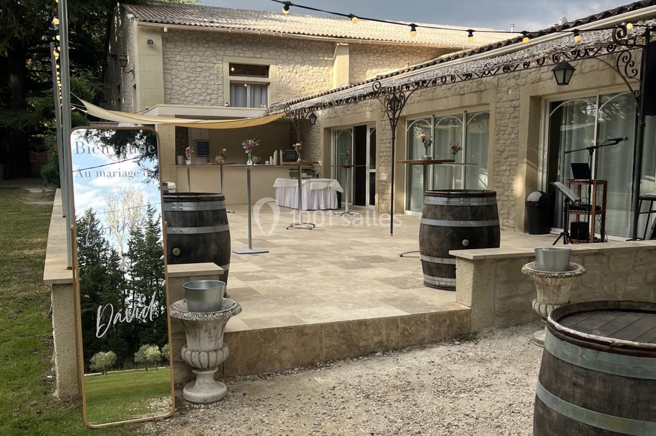 Terrasse en pierre avec décorations de mariage, tonneaux en bois, miroir de bienvenue et guirlandes lumineuses.