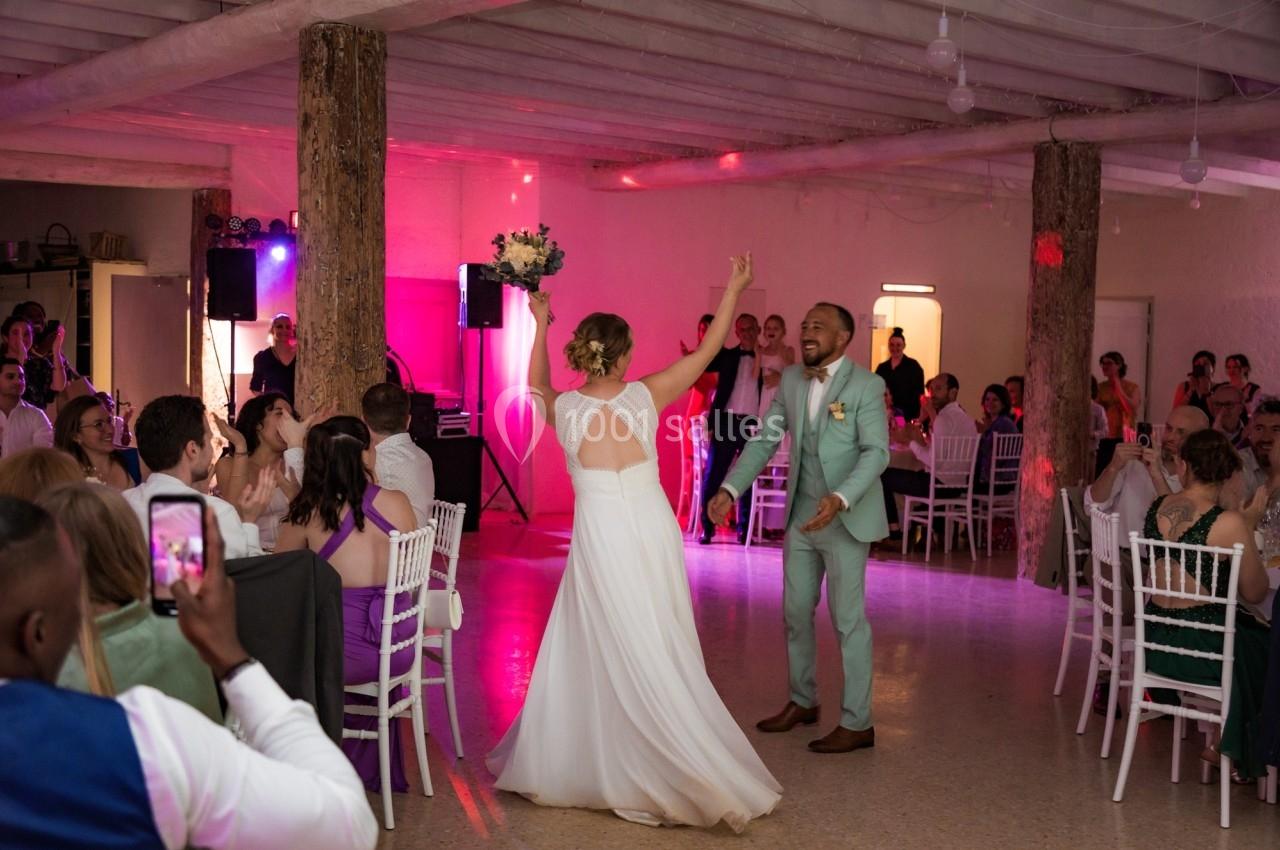 Un couple danse joyeusement au centre d'une salle de réception entouré d'invités assis et debout.