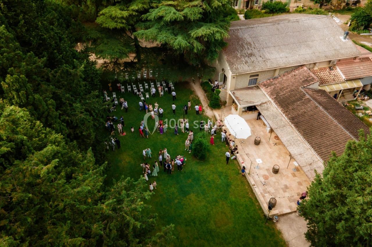 Vue aérienne d'un rassemblement de personnes dans un jardin entouré d'arbres, près de bâtiments en pierre.