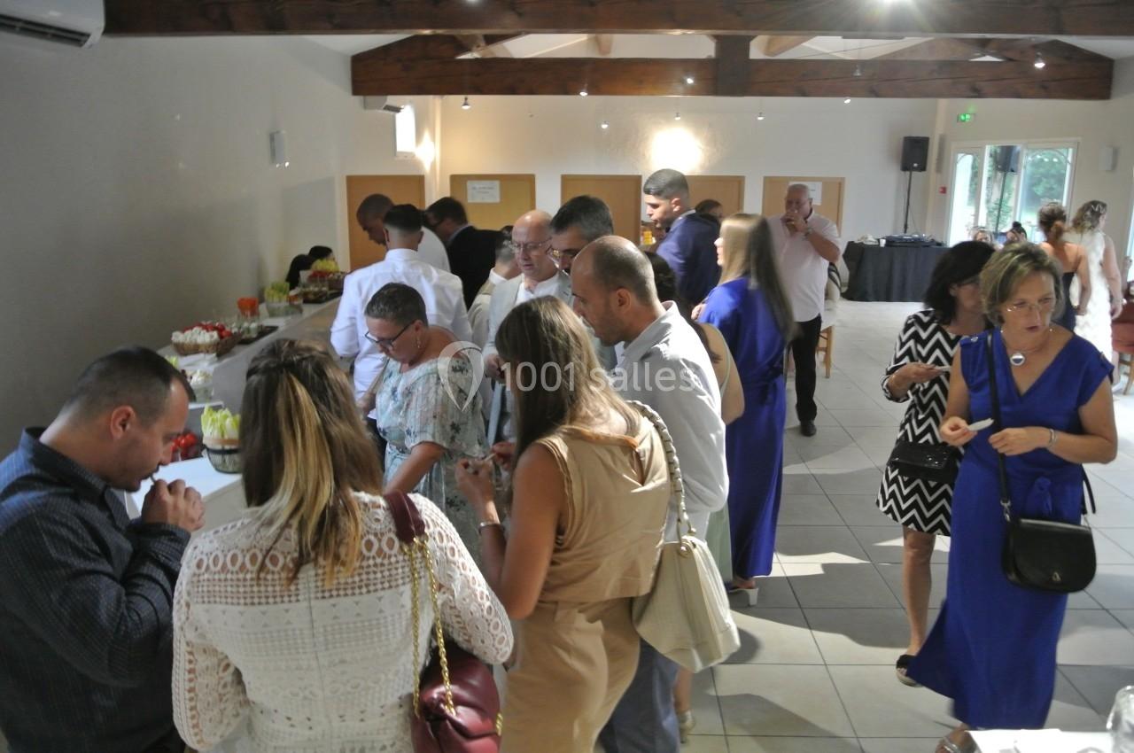 Des personnes se servent à un buffet dans une salle lumineuse avec des poutres apparentes et un sol carrelé.
