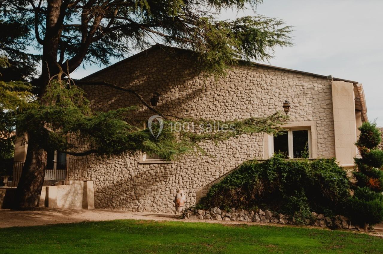 Façade en pierre d'une maison entourée d'arbres, avec une pelouse au premier plan.