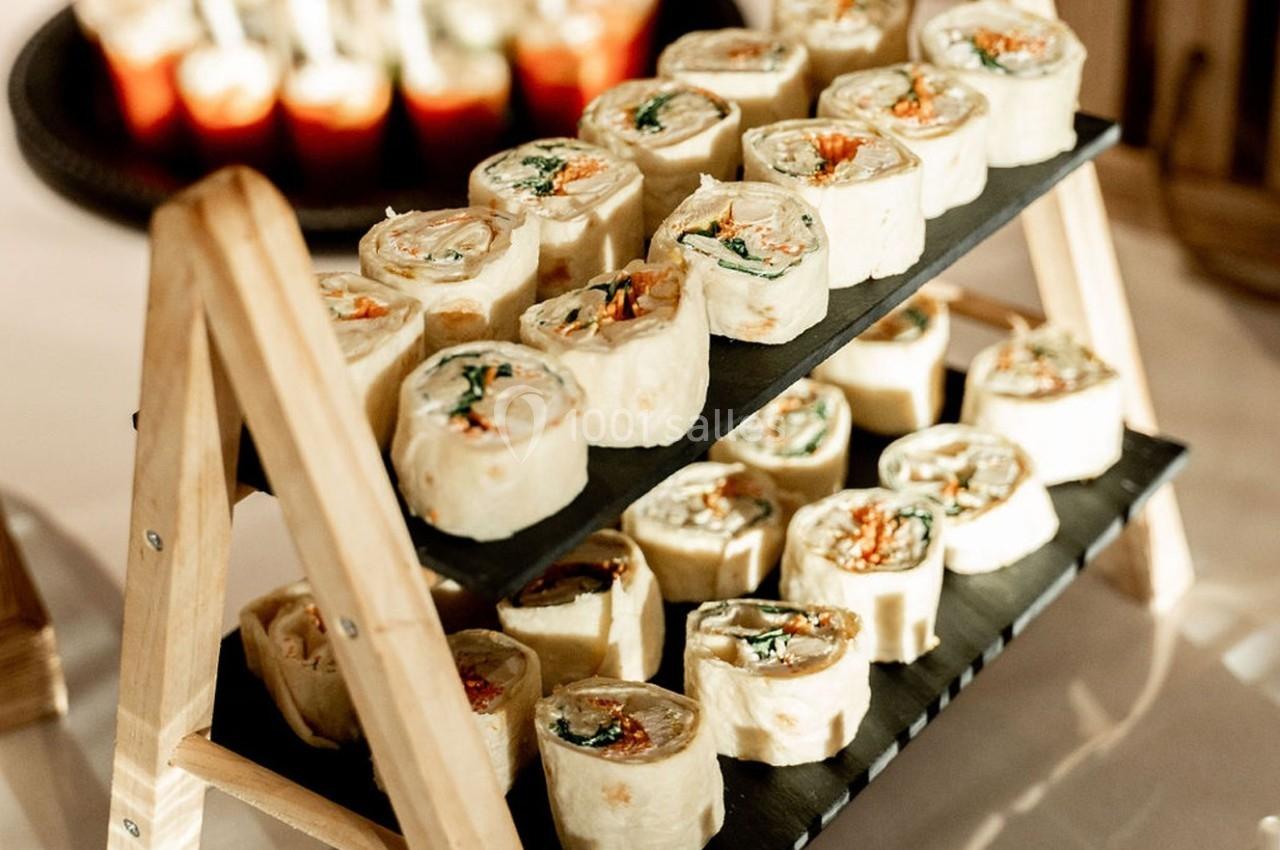 Plateau en bois avec des roulés apéritifs garnis de légumes et de fromage, disposés sur deux étages.