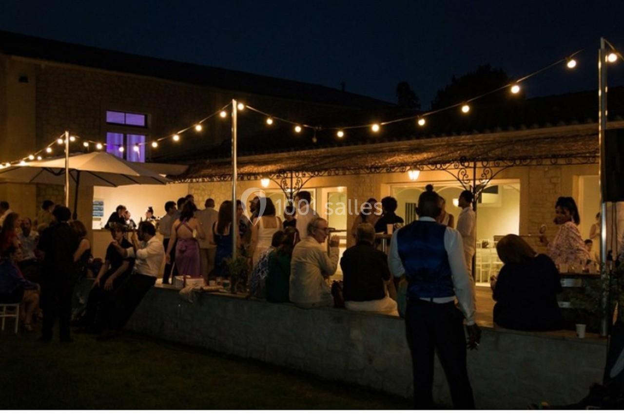 Groupe de personnes rassemblées en soirée dans une cour éclairée par des guirlandes lumineuses.