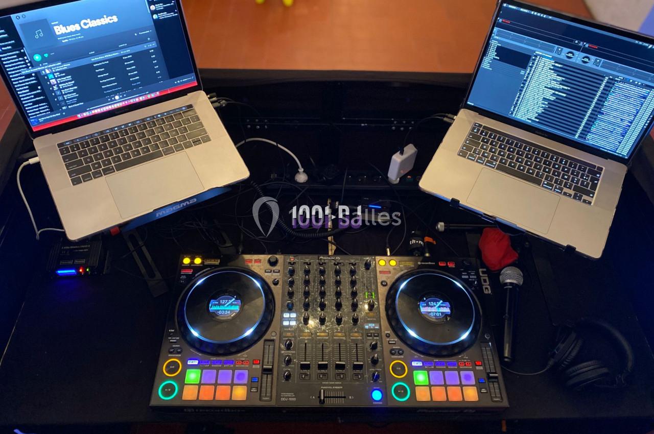 Deux ordinateurs portables et une console de mixage DJ avec des câbles et accessoires sur une table.