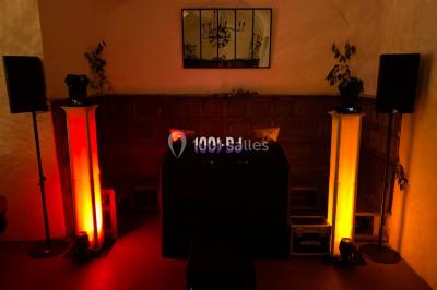 Salle de réception décorée avec des tables rondes éclairées en bleu, nappes blanches et bougies allumées.