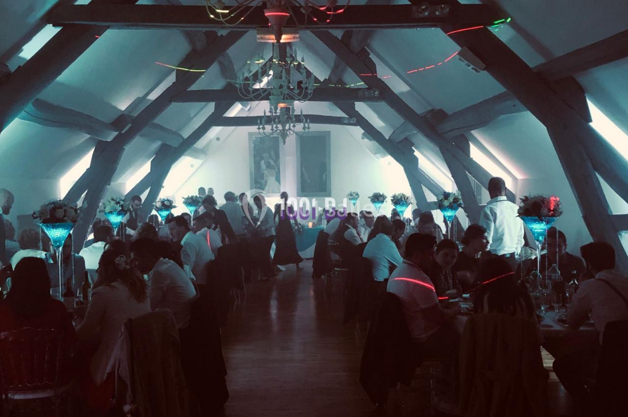 Salle de réception avec des invités assis à des tables décorées, éclairage tamisé et ambiance festive.