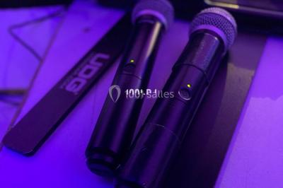 Salle de réception décorée avec des tables rondes éclairées en bleu, nappes blanches et bougies allumées.