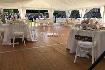 Salle de réception décorée avec des tables rondes éclairées en bleu, nappes blanches et bougies allumées.