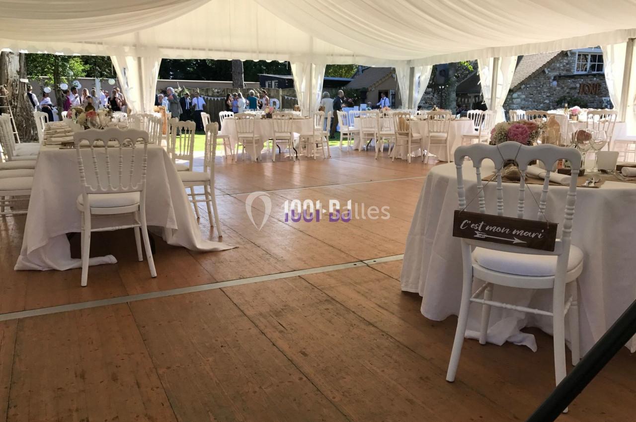 Intérieur d'une tente de réception avec tables et chaises blanches, décorée pour un événement en plein air.