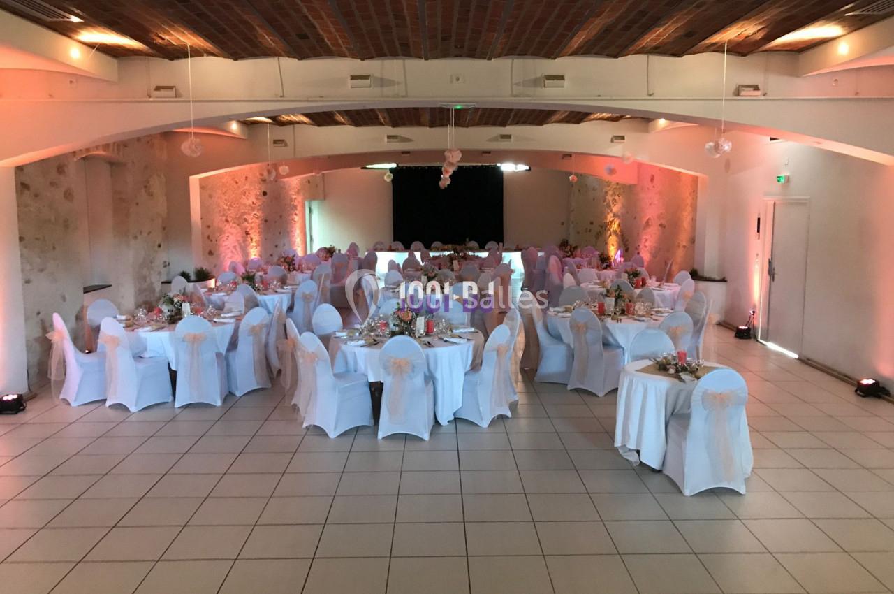 Salle de réception décorée avec des tables rondes, nappes blanches et chaises habillées, prête pour un événement.