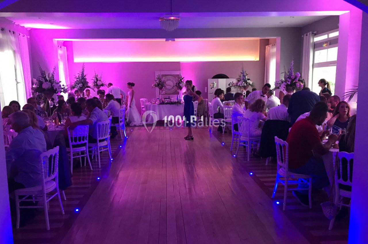 Salle de réception éclairée en rose avec des invités assis à des tables décorées, lors d'un événement festif.