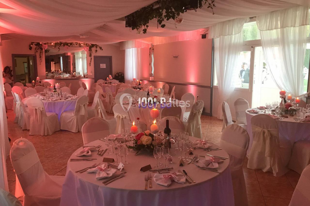 Salle de réception décorée avec des tables rondes dressées, nappes blanches, bougies et éclairage tamisé.