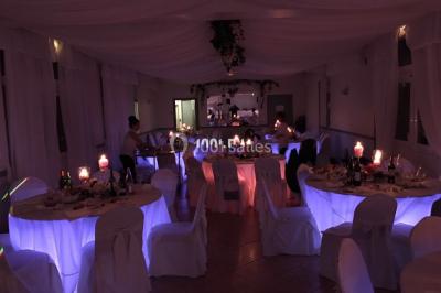 Salle de réception décorée avec des tables rondes éclairées en bleu, nappes blanches et bougies allumées.