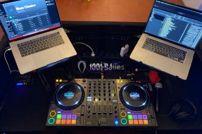 Salle de réception décorée avec des tables rondes éclairées en bleu, nappes blanches et bougies allumées.